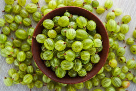 green fresh gooseberry berry in a bowl on wooden table. ripe fruit food. top viewの写真素材