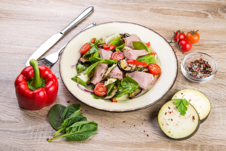 Fresh salad with ham, red pepper, eggplant and basil leaves, tomato on a wooden tableの写真素材
