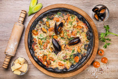 Black pizza with seafood and cheese on a wooden table. top viewの写真素材