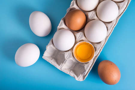 Homemade chicken eggs in a tray. One is broken. Blue background. Top viewの写真素材