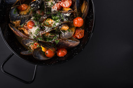 Shell mussels in a frying pan with chesse and sauce on a black background. top viewの写真素材