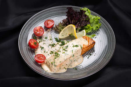 Fish steak salmon grilled with fresh salad and lemon on a black tableの写真素材