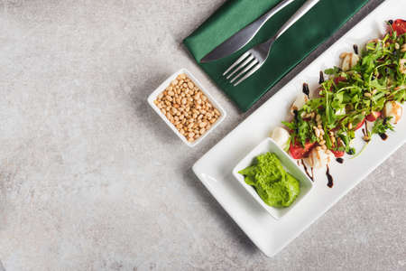 Fresh salad with mozzarella, sauce pesto and pine nuts on a stone table. top viewの写真素材
