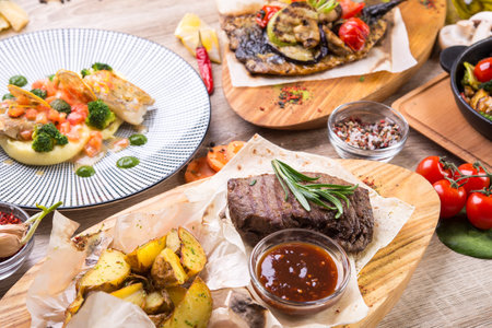 Table lined with dishes steak, roast beef in pan, mackerel with grilled vegetables on a wooden table. top view. flat layの写真素材