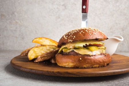 Tasty burger with knife and potato on a wooden boardの写真素材