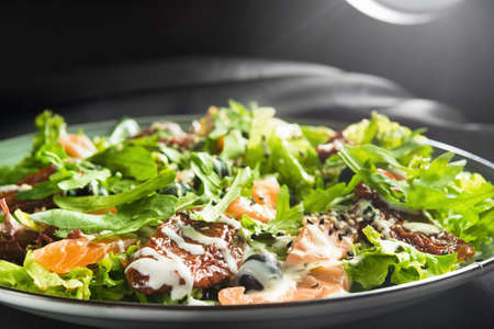 salad with salmon, dried tomatoes and green rucola on a black backgroundの写真素材