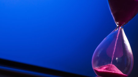 Bright colored pink sand with hourglass on a blue