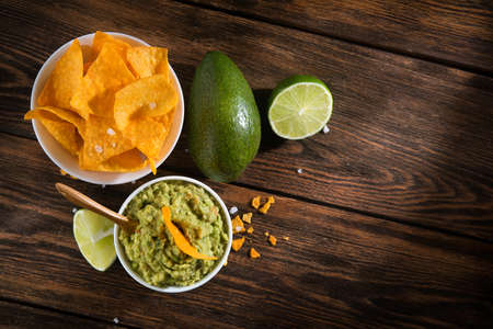 Bowl with guacamole sauce and nachos chips on a wooden tableの写真素材