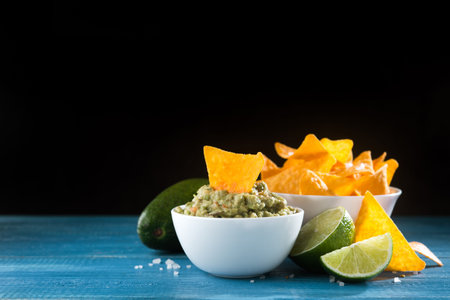 Bowl with guacamole sauce and nachos chips on a wooden table