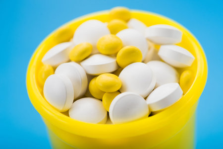Closeup of white and yellow vitamins pills in container on blue background