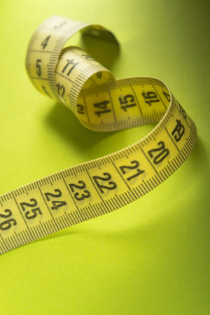 Closeup of yelllow measuring tape on a green background. Diet and weight loss