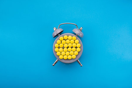 Yellow pills with time clock on a blue background. Time to take the medicine. Creative top view.