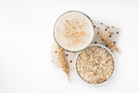 Glass of oat milk and grains in white bowl isolated on white background