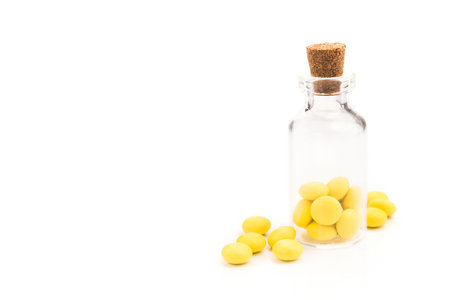 Yellow round vitamin pills in glass bottle isolated on a white background