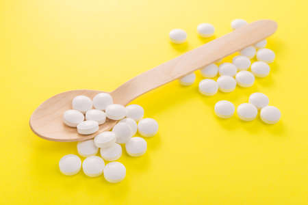 White medical pills and tablets at wooden spoon on a yellow backgroundの写真素材