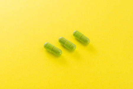 Three green capusle on a yellow background. Bright medical photo.