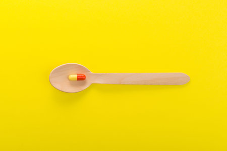 One super red and yellow capsule on a spoon, yellow background. minimalism concept. top view. space...