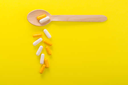 Pile of colored capsule pills on a yellow background. Bright medical photo. Concept minimalism and simplicity. top viewの写真素材