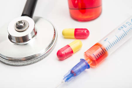 Stethoscope, ampule of red medicine, syringe and pills isolated on a white background. Treatment of heart disease.の写真素材