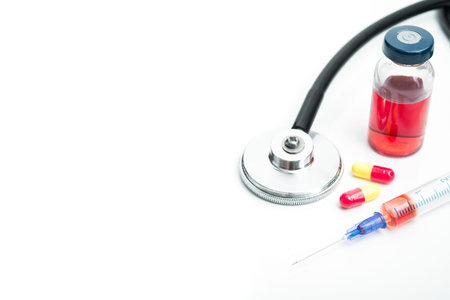 Stethoscope, ampule of red medicine, syringe and pills isolated on a white background. Treatment of...