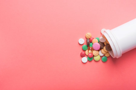 White bottle of medical colored pills and capsule on a pink pastel background. top view. place for...