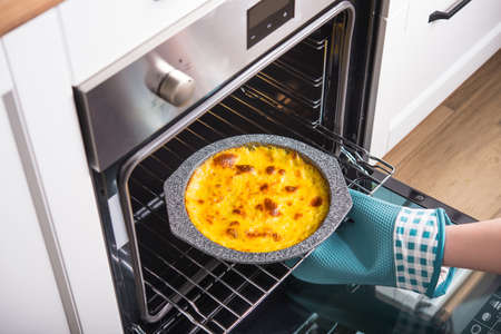 Woman gets a cottage cheese cake from the oven. Sweet baked dessert. Cooking in the kitchen.の写真素材