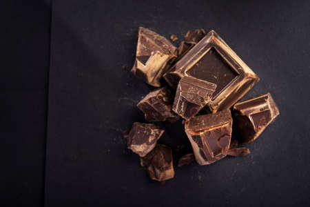 Pieces of tasty black chocolate on a black paper background. Sweet and calorie food. top view. copy spaceの写真素材