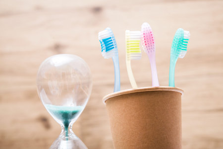 Four toothbrushes in a paper cup with hourglass in the bathroom. hygiene and teeth cleaning.