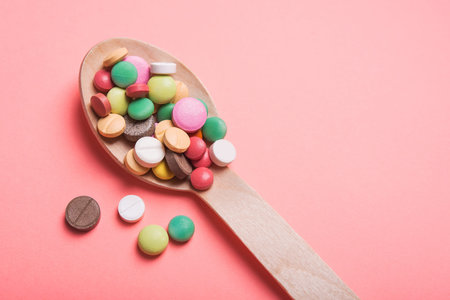 Wooden spoon with medicine pills and tablets on a pastel pink background. top view. place for text.