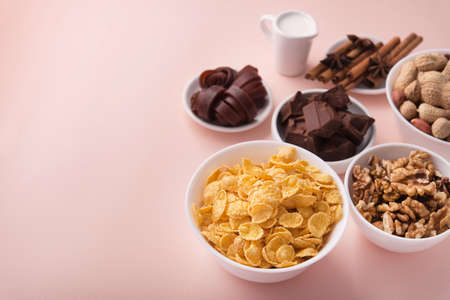 Delicious breakfast ingredients cornflake, chocolate, paste, nuts, peanuts on a pink pastel background. place for textの写真素材