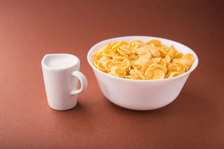 Bowl with cornflakes, milk carafe on a brown pastel background. cereal healthy morning breakfast.の写真素材