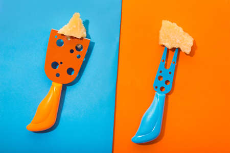 Creative concept of two pieces of parmesan cheese on unique knives. Colored blue and orange flat lay. Top viewの写真素材
