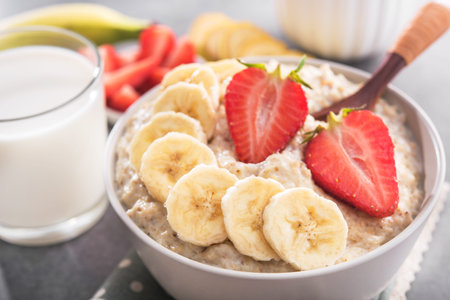 Oatmeal bowl with banana and strawberry, milk glass in a stone table. healthy organic food.の写真素材