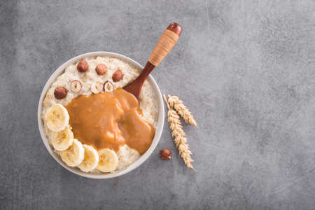 Sweet breakfast with bowl oatmeal, banana, nuts and caramel fudge on a stone table. Top view.の写真素材