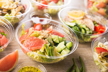 Plastic take away container with fresh salad consists of cucumber, avocado, tomato, grapefruit, on a wooden background. Tasty lunch food.の写真素材