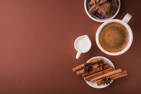 Coffee cup with milk carafe, chocolate pieces, spice cinnamon and badian on a color brown background. Top view. Copy space.の写真素材
