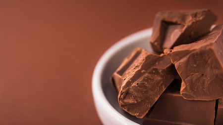 Pieces of chocolate in a white bowl on brown color background. place for text. banner format
