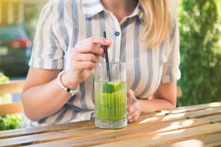 Young beautiful girl drinking cold drink beverage cocktail outdoors in cafe wooden table. Summer lifestyle people.の写真素材