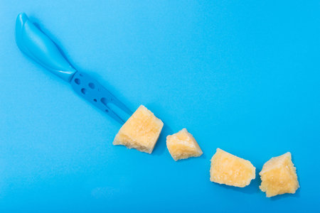 Tasty parmesan yellow cheese pieces on a blue background. Color and minimal concept.の写真素材