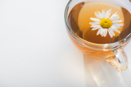 Glass cup with herbal tea with chamomile flowers on a white background. Healthy drink. place for...