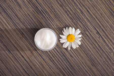 Container with chamomile cream and flowers on a table. cosmetic skin and body care concept. top viewの写真素材