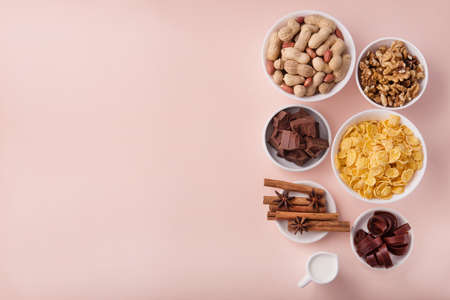 Delicious breakfast ingredients cornflake, chocolate, paste, nuts, peanuts on a pink pastel background. Top view. place for textの写真素材