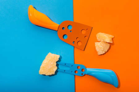 Creative concept of two pieces of parmesan cheese on unique knives. Colored blue and orange flat lay. Top viewの写真素材
