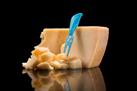 Tasty and fresh pieces of Parmesan cheese on a partitioning wooden board, black background.
