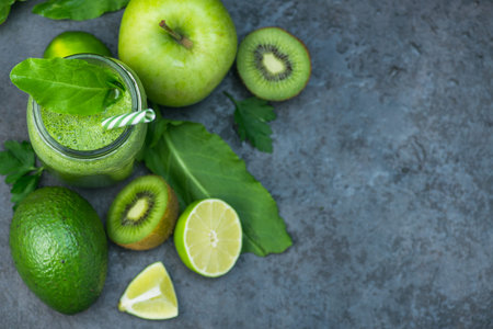 Green detox smoothie in glass jar from spinach, kiwi, lime, avocado on a dark stone table. Diet and...