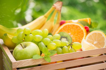 Basket of fresh fruits with banana, apple, grapes, green kiwi in the garden background. Healthy and Vitamin Food. Summer harvest.の写真素材
