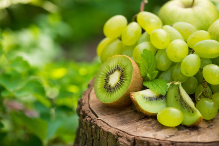 Fresh natural green fruits apples, grapes, kiwi and mint leaf on a wooden stump in garden. harvesting outdoors eating.の写真素材