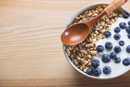 Bowl of homemade granola with yogurt, fresh blueberry and wheat seeds on a wooden table. healthy...