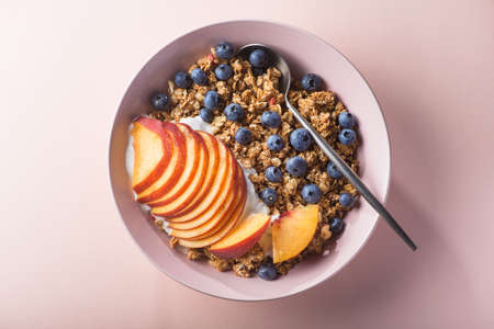 Bowl of granola with yogurt, peach slices and bluberry on a pastel pink background. Morning food dessert. Healthy breakfast snack. top viewの写真素材
