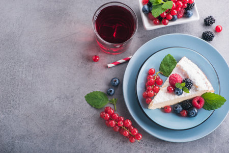 Sweet dessert cake with fresh blackberry, raspberry, currants and blueberry and green mint, red lemonade berry drink on stone table. copy space text. top viewの写真素材
